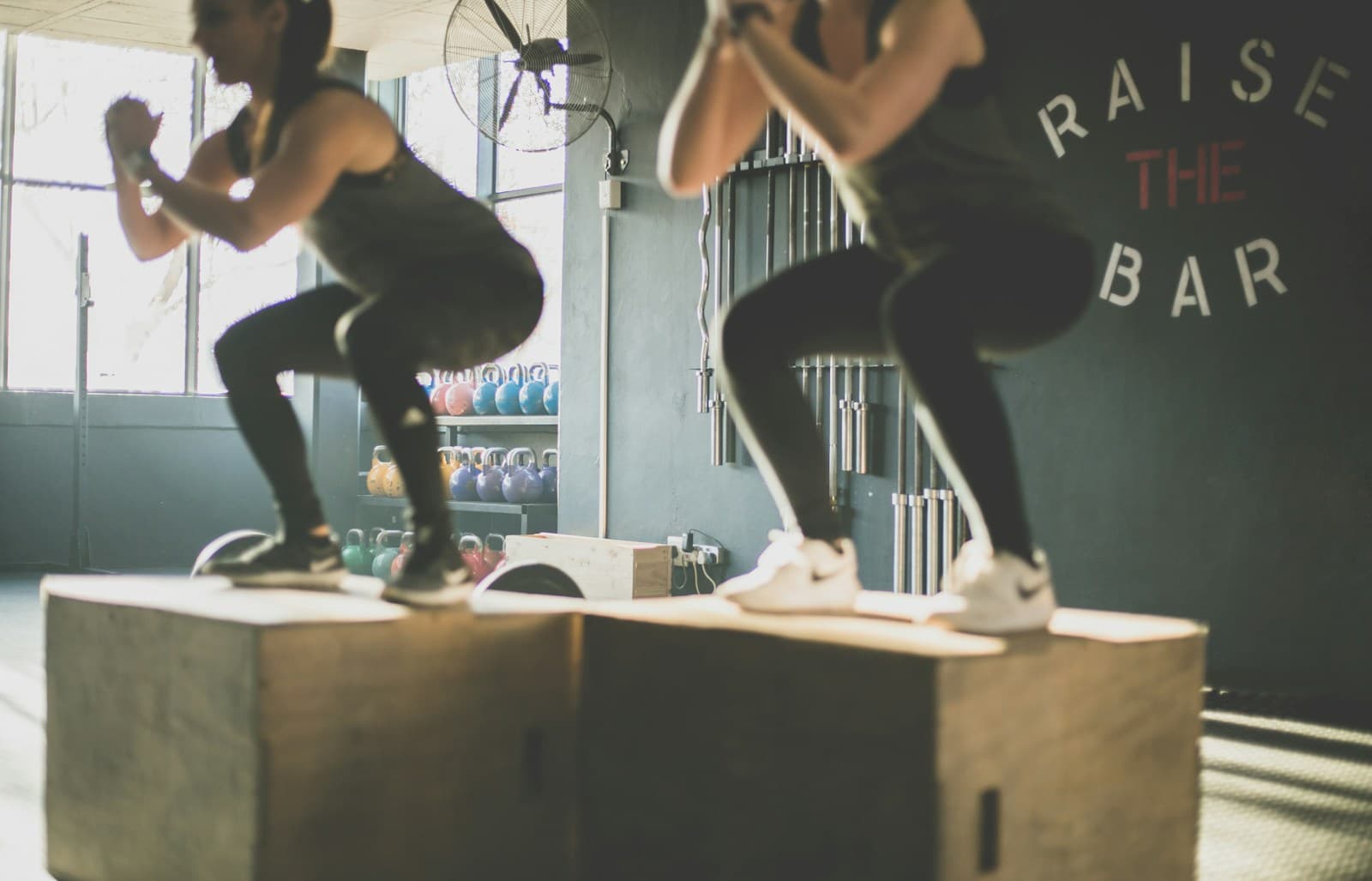 Dos personas aterrizando un salto al cajón, con kettlebells de fondo